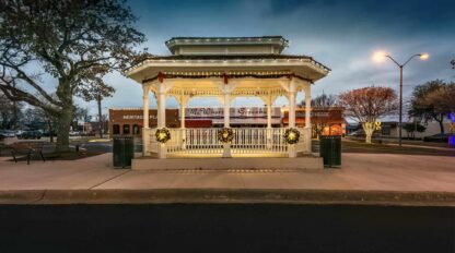 A gazebo sits in the middle of a street at night.