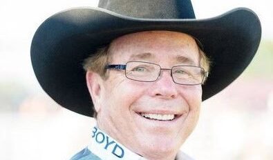 A man wearing a cowboy hat and glasses smiles.