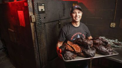 A man holding a tray of ribs in front of an oven.
