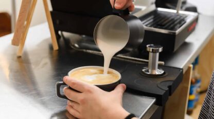 A person pouring milk into a cup of coffee.
