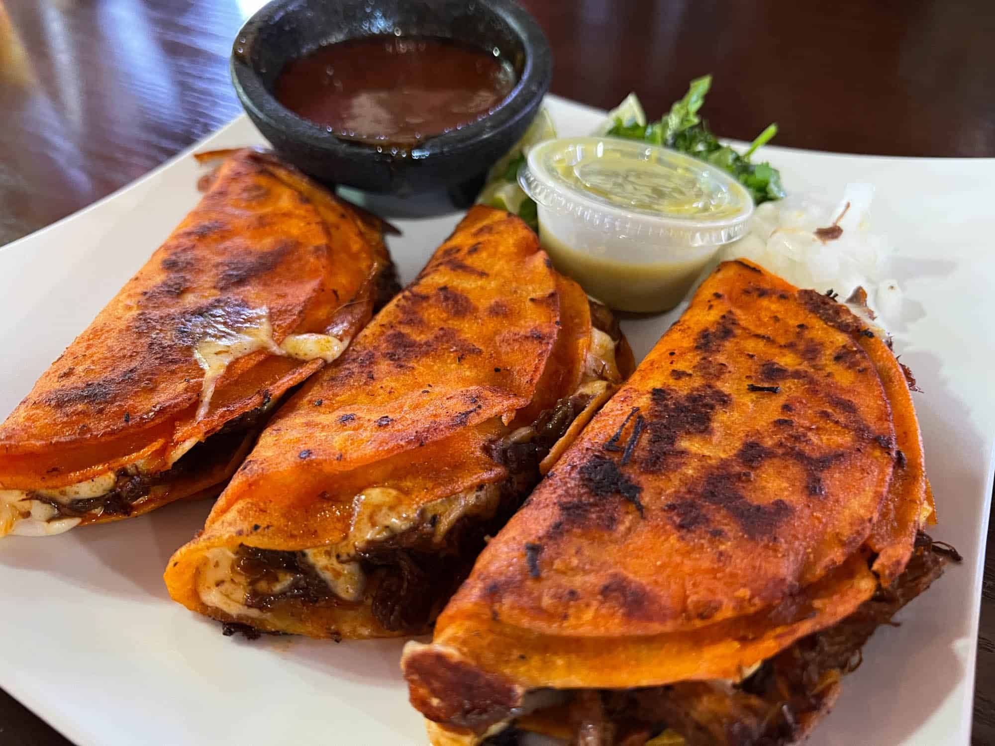 Three quesadillas on a plate with dipping sauce.