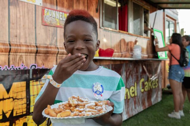 A young boy holding a plate of food in front of a food truck.