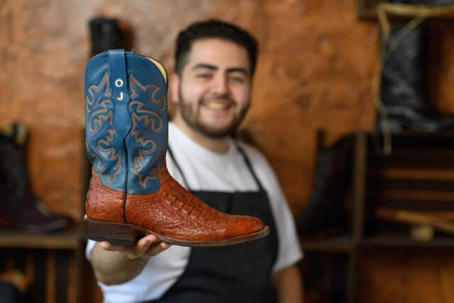 A man holding up a pair of cowboy boots.