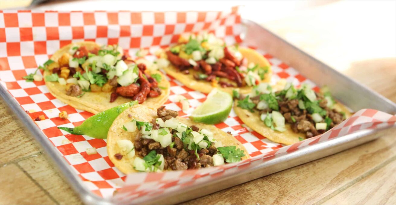 Four tacos on a tray on a wooden table.