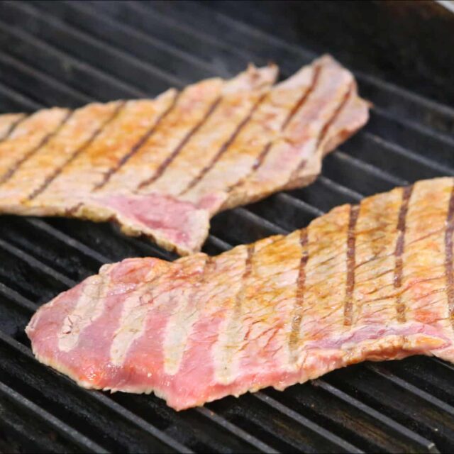Two steaks are being cooked on a grill.