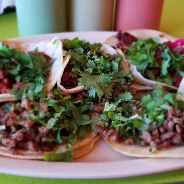Four tacos on a plate on a green table.