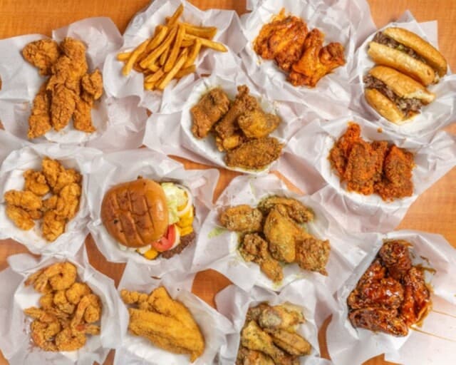 An assortment of fried chicken, wings, fries, sandwiches, and a burger are arranged in paper-lined baskets on a wooden table.