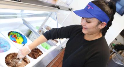 A smiling employee scooping ice cream at a parlor.