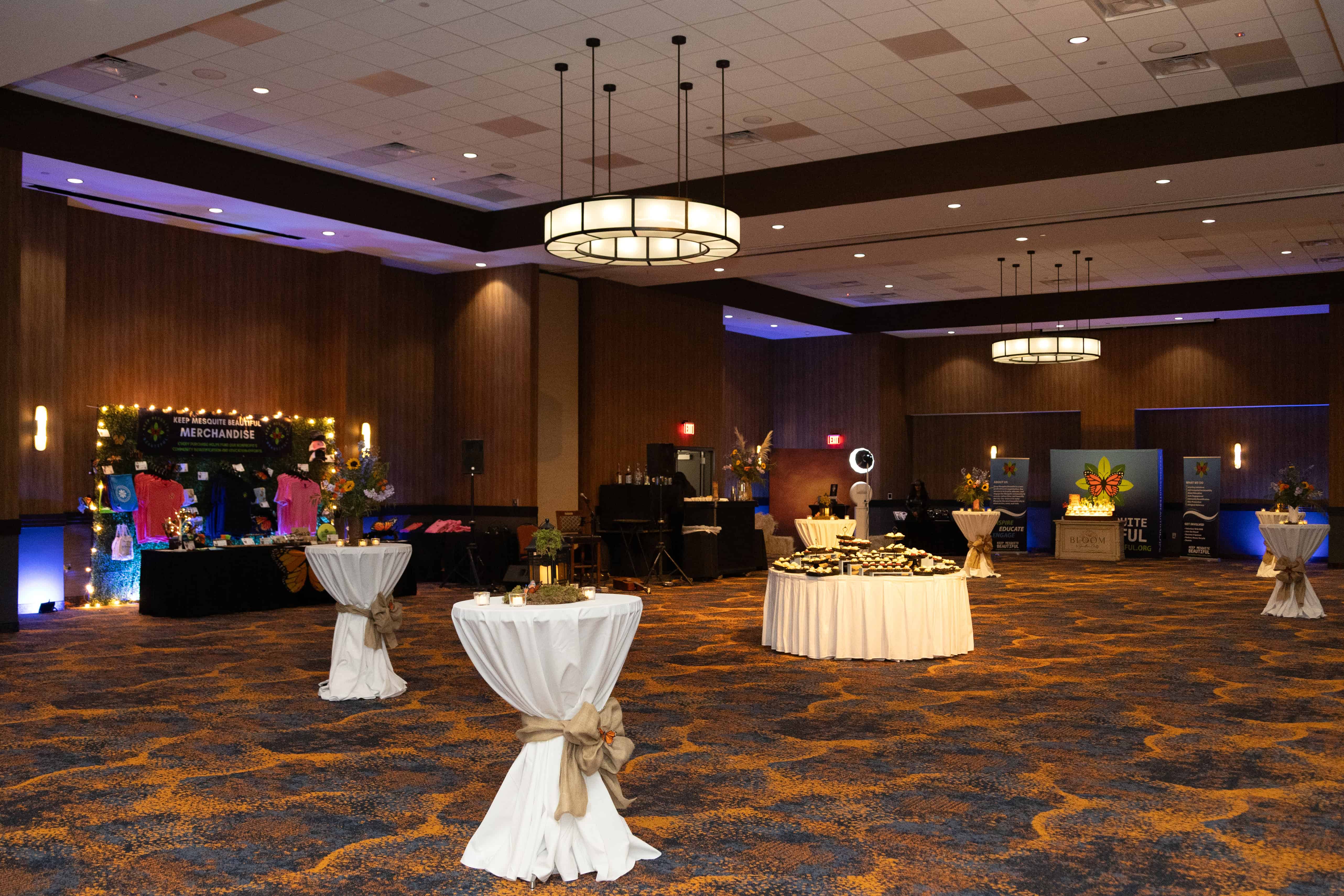 A hotel ballroom arranged for an event with tall cocktail tables, a larger round table with food, and branded banners for Keep Mesquite Beautiful.