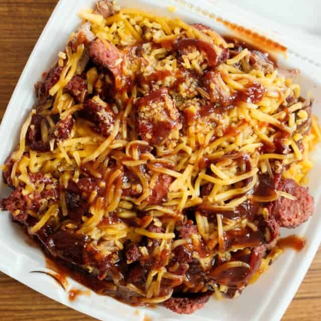 Takeout container filled with chopped beef, shredded cheese, and barbecue sauce on a wooden table.