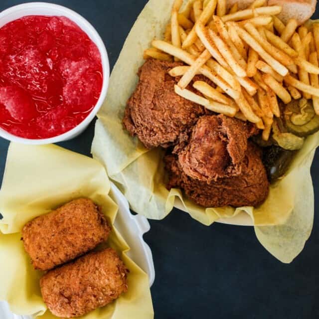 Basket with fried chicken, fries, and pickles; a side of two breaded items in another container; cup of red slush drink.