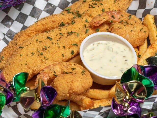 A plate of fried fish and shrimp with fries, served with a side of tartar sauce. The basket is decorated with colorful metallic beads.