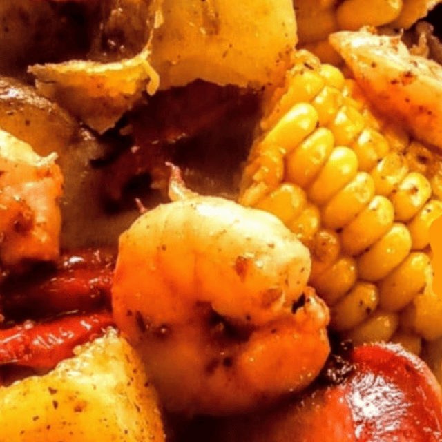 Close-up of a seafood boil featuring shrimp, corn on the cob, and pieces of sausage seasoned with spices.