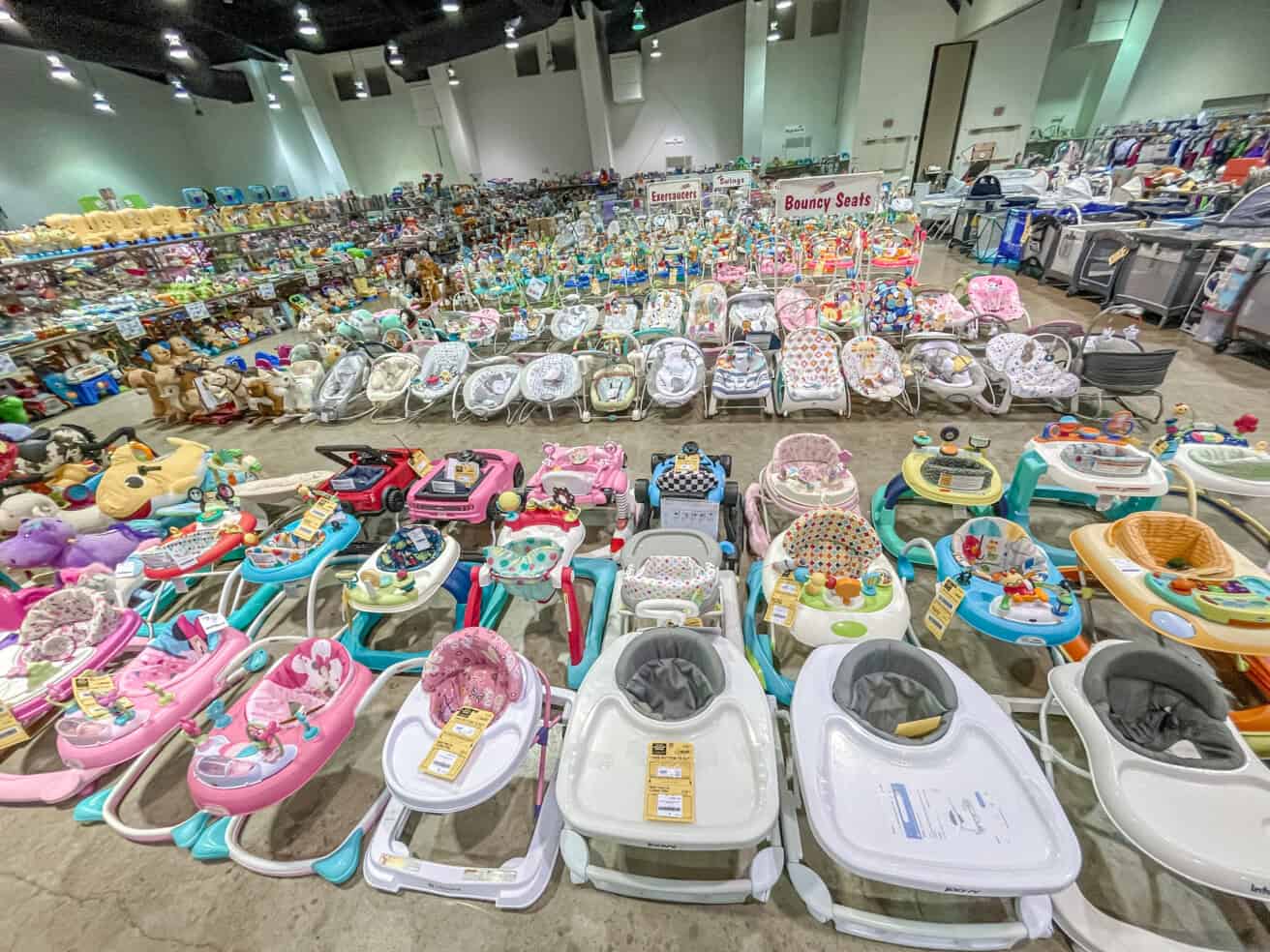 A large selection of baby walkers and related merchandise displayed in rows at an indoor sale event.