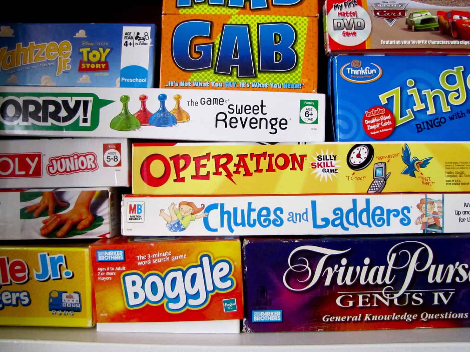 A shelf stacked with various board games, including Operation, Chutes and Ladders, Sorry!, Trivial Pursuit, Boggle, and others.