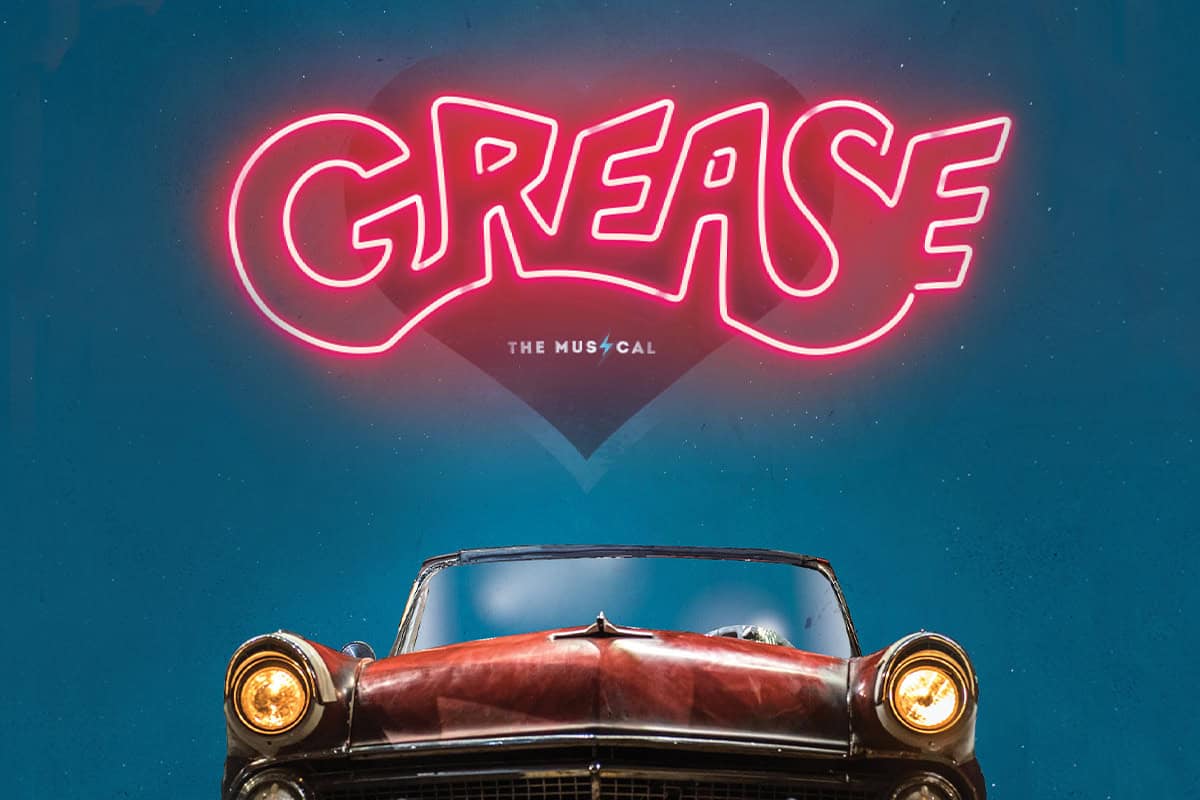 A classic convertible car is at the bottom of the image, with the word "GREASE" in bold, pink neon letters above it and "The Musical" written underneath.