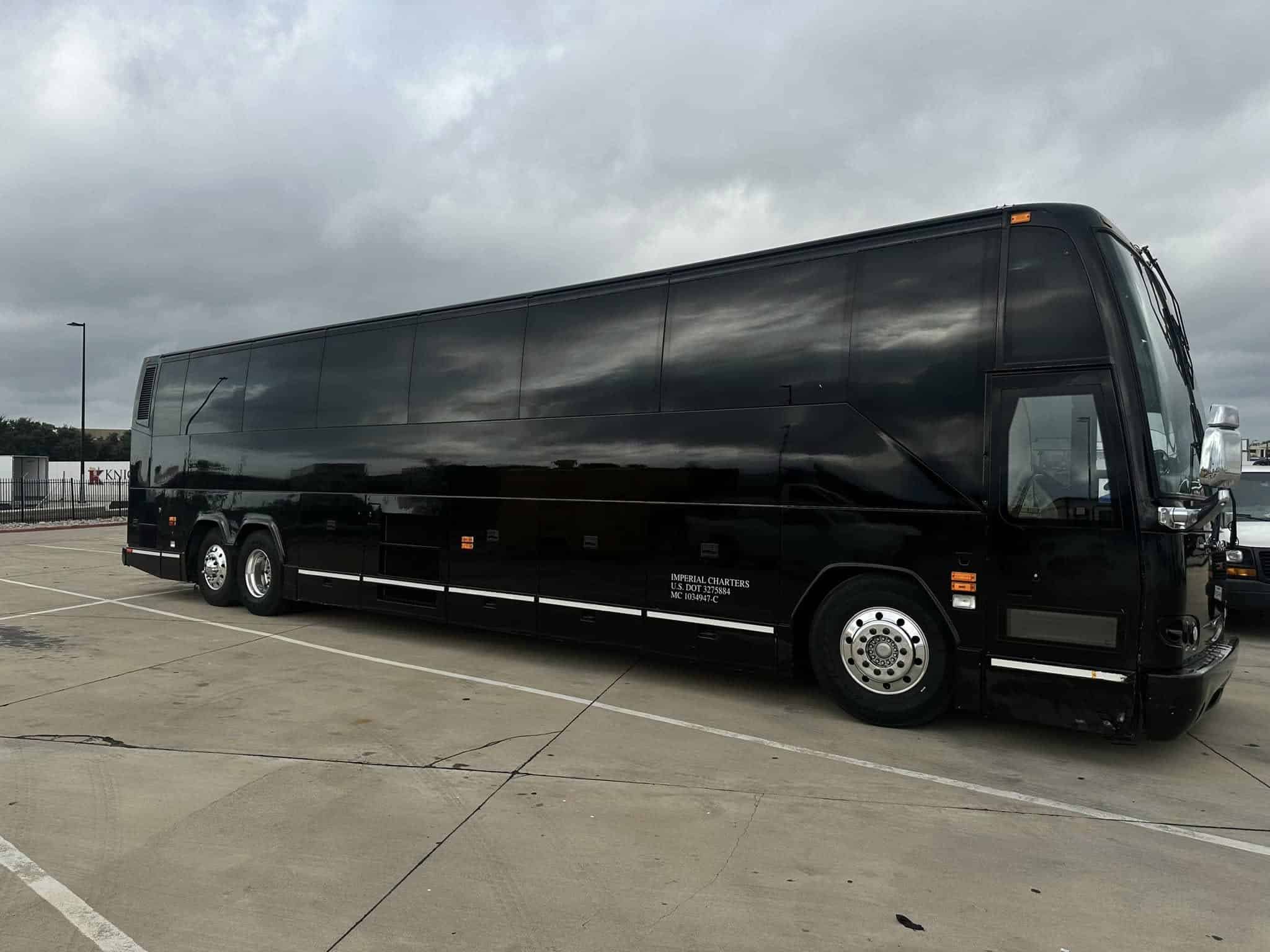 A large, black tour bus is parked in an empty, paved lot under a cloudy sky.