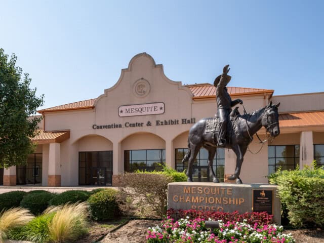 Statue of a rodeo rider on horseback in front of the Mesquite Convention Center and Exhibit Hall, with "Mesquite Championship Rodeo" inscribed on a sign.